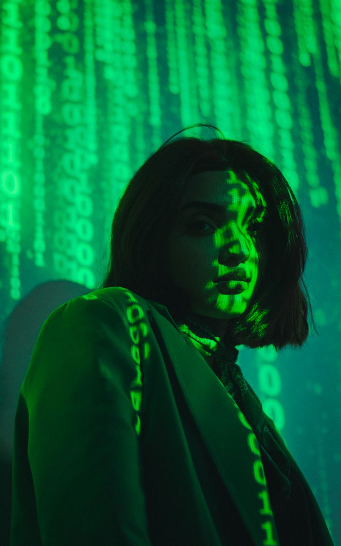 A woman stands under a cascading green binary code projection, evoking a cyberpunk aesthetic.